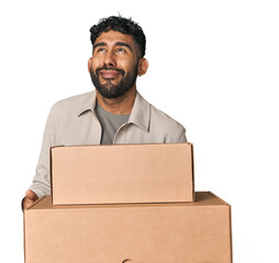 Hispanic male holding cardboard boxes in studio dreaming of achieving goals and purposes