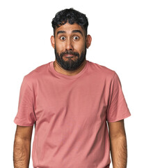 Young Hispanic man isolated shrugs shoulders and open eyes confused.