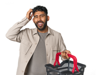Hispanic male holding shopping basket in studio being shocked, she has remembered important meeting.