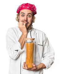 Young chef holds pasta sauce jar in studio biting fingernails, nervous and very anxious.