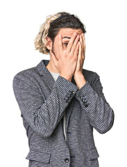 Young businessman in casual blazer blink through fingers frightened and nervous.