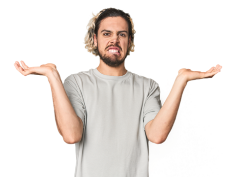 Young Caucasian man in studio setting confused and doubtful shrugging shoulders to hold a copy space.