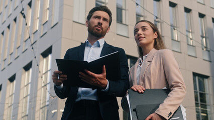 Two business people man and woman communicate in city near office holding folder papers documents male boss talking with female manager discuss work project corporate businessman with businesswoman