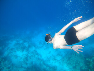 Boy snorkeling dive deep into the blue sea near the coral reef. Red Sea