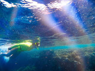 A woman in a green swimsuit and mask swims underwater exploring the corals of the Red Sea. Snorkeling