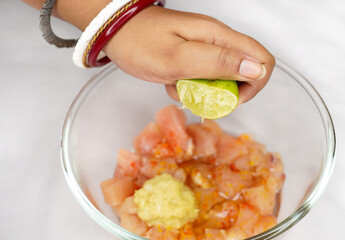 Indian woman adding lemon onto chicken pieces for cooking. closeup