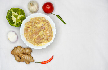 White bowl with marinated chicken pieces and other ingredient over white background and copy space.