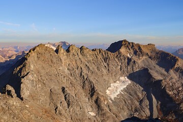 Aerial view of rocky mountain range with snow patches under a clear blue sky day