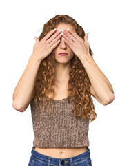 Simple redhead studio portrait afraid covering eyes with hands.