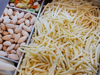 Close-up shot of frozen french fries and other frozen food items in metal trays.