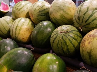 A pile of watermelons of varying sizes and shades of green, some showing yellowing, displayed at a market or grocery store.  The image is close up and focuses on the texture and color of the fruit.