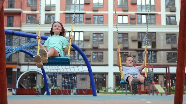 Happy children, boys and girls, ride on a swing on a modern playground.