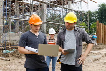 Construction engineers using laptop and tablet to discuss project progress at building site. Team collaboration in civil engineering and site supervision concept.