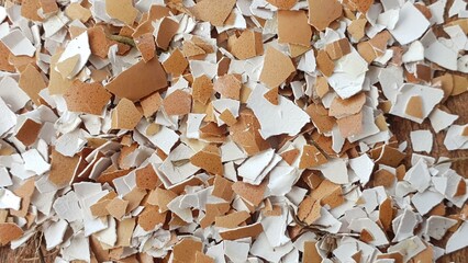Close-up shot of crushed eggshells, showcasing a mix of brown and white fragments. The texture is rough and varied.