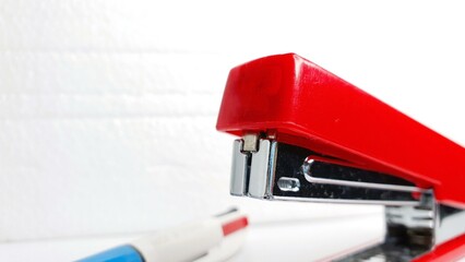 Close-up shot of a red stapler on a white background.  A blurred pen is in the foreground.