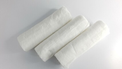 Three rolls of white gauze bandages on a white background.  Clean, sterile, medical supplies.