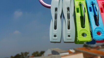 Colorful clothespins hanging against a bright blue sky.  A blurry background shows houses and trees.