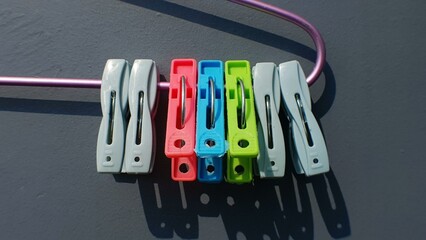 Colorful clothespins hanging on a purple hanger against a dark gray background.