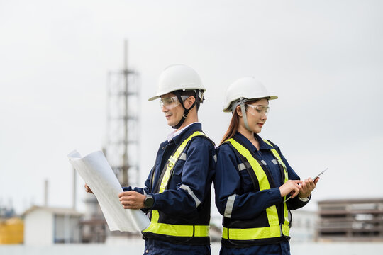 Male and Female Engineers Standing Back-to-Back, Symbolizing Teamwork and Partnership. Two people wearing safety gear and holding papers - Powered by Adobe