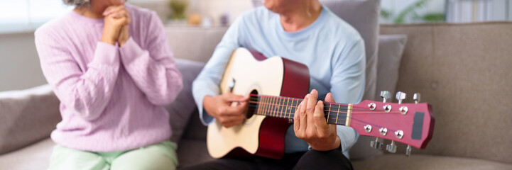 Older Asian Couple Enjoying Music At Home Senior Man Playing Guitar for Wife Relaxing Together...