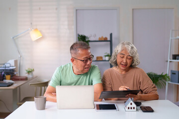 Senior Asian Couple Planning Retirement Savings and Investments in Home with Tablet, Laptop, and...
