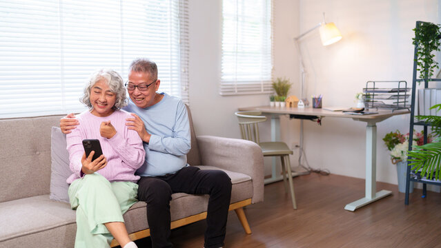 Happy Asian Senior Couple Relaxing at Home Watching Funny Videos on Phone Together Older Couple Enjoying Time Together Laughing and Bonding Through Modern Technology