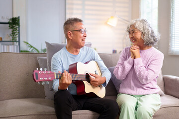 Senior Asian Couple Enjoying Music at Home Older Man Plays Guitar for his Loving Wife Happy Elderly People Spend Quality Time Together in Cozy Living Room