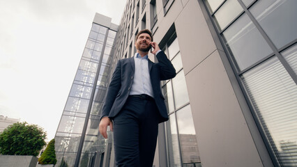 Middle-aged Caucasian business man calling mobile phone talking call walking going near office building in city businessman male talk smartphone work job discuss negotiation serious entrepreneur walk