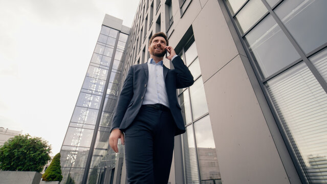 Middle-aged Caucasian business man calling mobile phone talking call walking going near office building in city businessman male talk smartphone work job discuss negotiation serious entrepreneur walk - Powered by Adobe