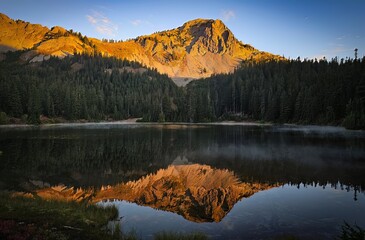 Mountain peak reflecting in a lake surrounded by evergreen trees at sunset time