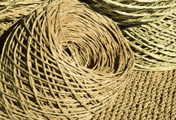 Natural raffia fibers are wound into spools against a crocheted background. The spools are beige and craft colors.