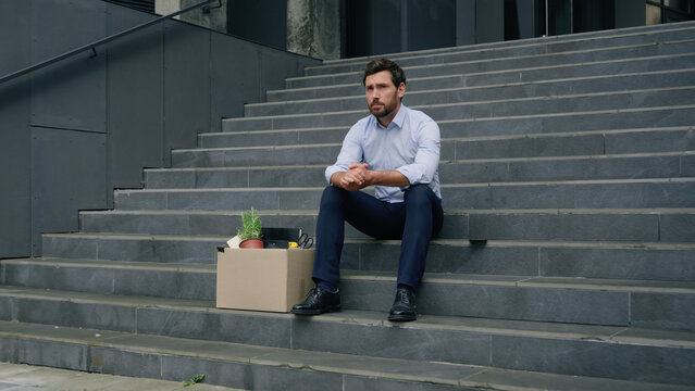 Stressed Caucasian middle aged business man lost job fired work sitting stairs near office building with dismissal box businessman male suffering sad thinking trouble crisis financial failure dismiss - Powered by Adobe
