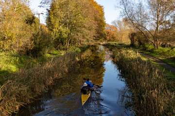 Two people in a kayak paddle down a beautiful stretch of the River Wey Navigation canal in Autumn