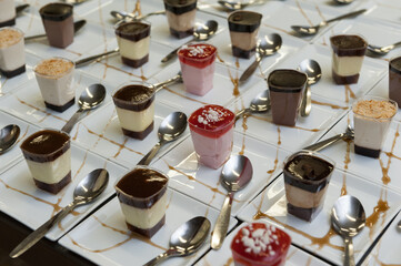 A variety of pudding cups on small white ceramic plates with silver spoons prior to serving dessert at a wedding banquet.