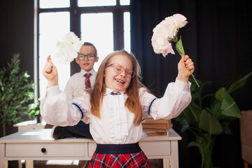 A 7-year-old child in glasses dressed in  school uniform poses at the school table indoor