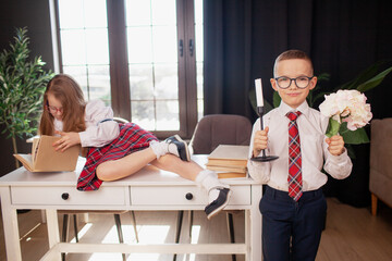 A 7-year-old child in glasses dressed in  school uniform poses at the school table indoor