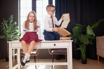 A 7-year-old child in glasses dressed in  school uniform poses at the school table indoor