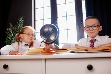 A 7-year-old child in glasses dressed in  school uniform poses at the school table indoor