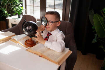 A 7-year-old child in glasses drssed school uniform poses at the school table indoor