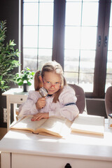 A 7-year-old child in glasses dressed in school uniform poses at the school table indoor. The girl holds globe