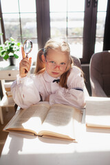 A 7-year-old child in glasses dressed in school uniform poses at the school table indoor. The girl holds globe