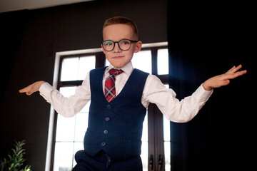 A 7-year-old child in glasses and dressed  school uniform poses at the school table indoor