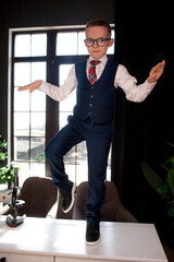A 7-year-old child in glasses and dressed  school uniform poses at the school table indoor