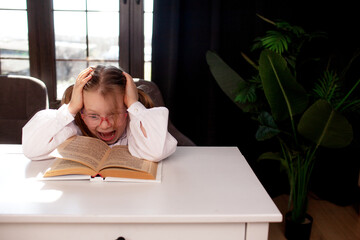 A 7-year-old child in glasses and dressed  school uniform poses at the school table indoor