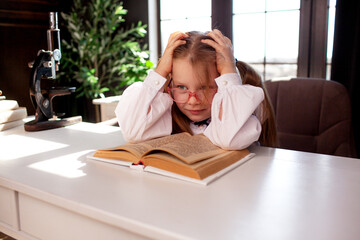A 7-year-old child in glasses and dressed  school uniform poses at the school table indoor