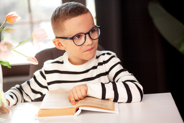 A 7-year-old child in glasses and dresses striped vest, poses at the school table indoor.