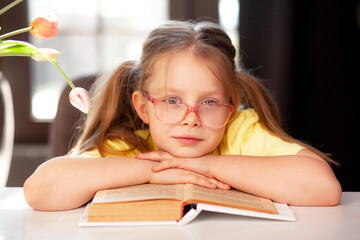 A 7-year-old child in glasses and  poses at the school table indoor