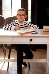 A 7-year-old child in glasses and school uniform poses at the school table indoor