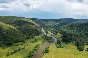 Aerial view of a meandering river winding its way through a picturesque valley, surrounded by lush...
