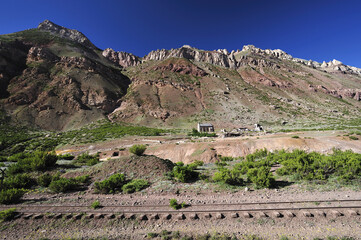A lonely house on the edge of a railway line through mountainous terrain. A dilapidated stone house abandoned at the foot of a thundering, rocky mountain